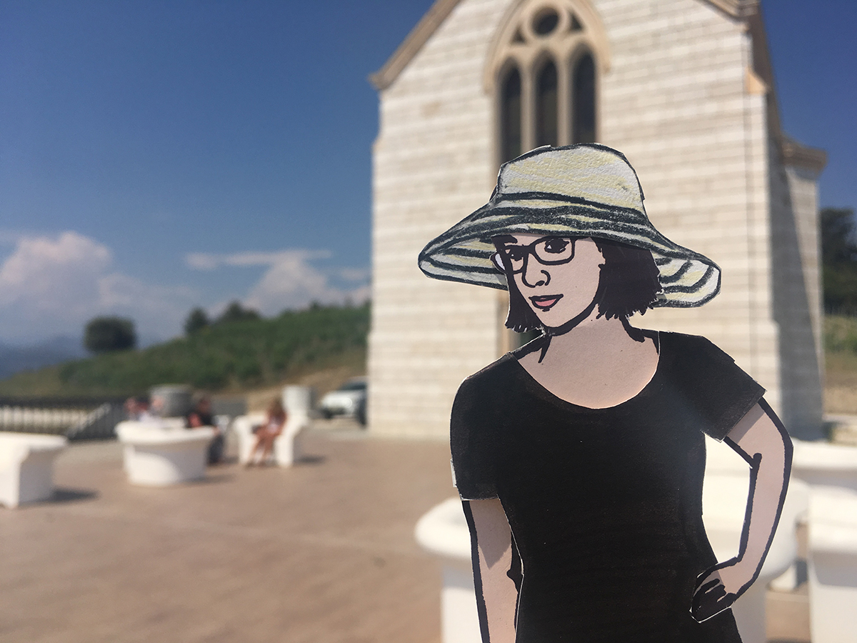 paper doll of the artist in front of chapel at a french winery
