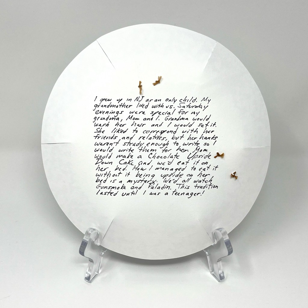 back of plate with letterpress printed hand-written text and evidence of cake-crumb colored stitching from for front side. Text in paragraph following. 